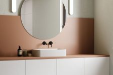 a minimalist neutral bathroom with sleek cabinetry, a terracotta backsplash, a round mirror and a neutral sink