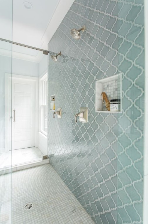 a modern bathroom with neutral tiles on the floor and a blue arabesque tile accent wall with niches for storage is a very stylish and cool idea