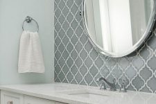a modern farmhouse bathroom with grey arabesque tiles for an accent, white planked vanities, a round mirror and a simple towel