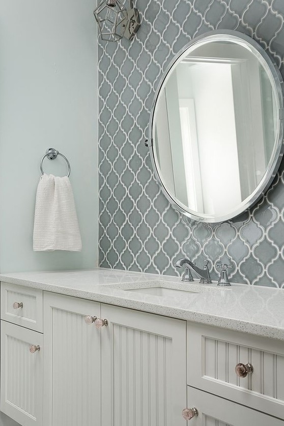 a modern farmhouse bathroom with grey arabesque tiles for an accent, white planked vanities, a round mirror and a simple towel