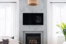 a modern farmhouse living room with a concrete fireplace, a TV, a woven pendant lamp and neutral seating furniture, a printed rug