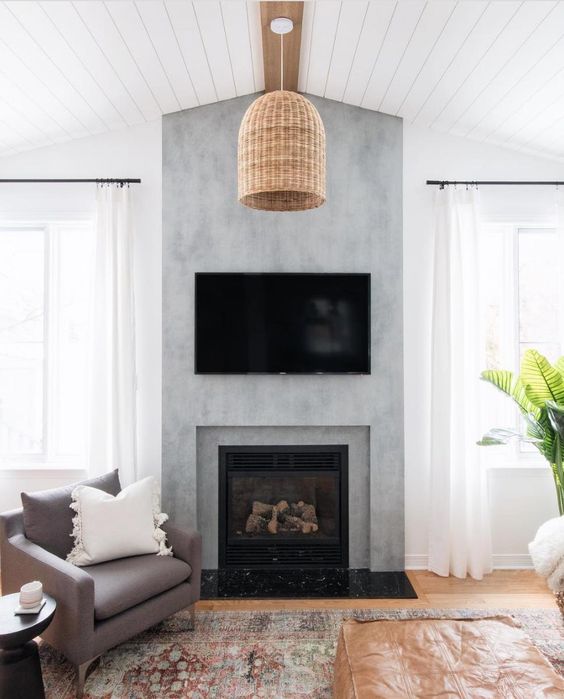 a modern farmhouse living room with a concrete fireplace, a TV, a woven pendant lamp and neutral seating furniture, a printed rug
