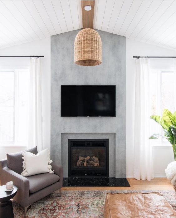 a modern farmhouse living room with a concrete fireplace, a TV, a woven pendant lamp and neutral seating furniture, a printed rug