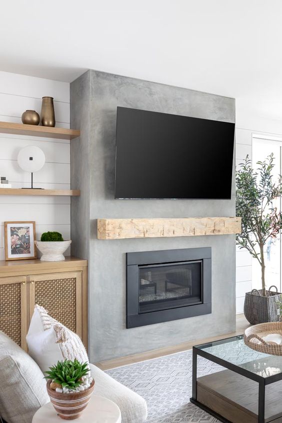 a modern farmhouse living room with a concrete wall and a built-in fireplace, a TV and neutral seating furniture plus potted plants