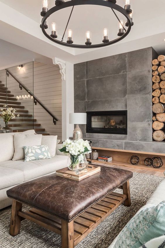 a modern living room with a fireplace and firewood storage, neutral seating furniture, a leather ottoman and printed textiles