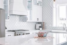 a modern white kitchen with black handles, a large white hood, a white arabesque tile backsplash and a wall is elegant