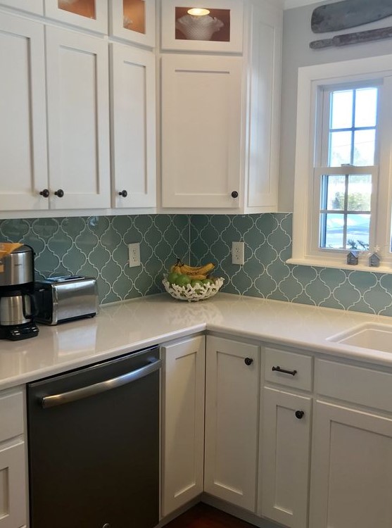 a modern white kitchen with black knobs and a blue arabesque tile backsplash plus white grout that accents the tiles