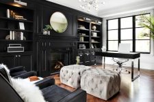 a moody home office with a glazed wall, a black storage unit with built-in shelves and a fireplace, a black desk and grey poufs, black chairs and a lovely chandelier