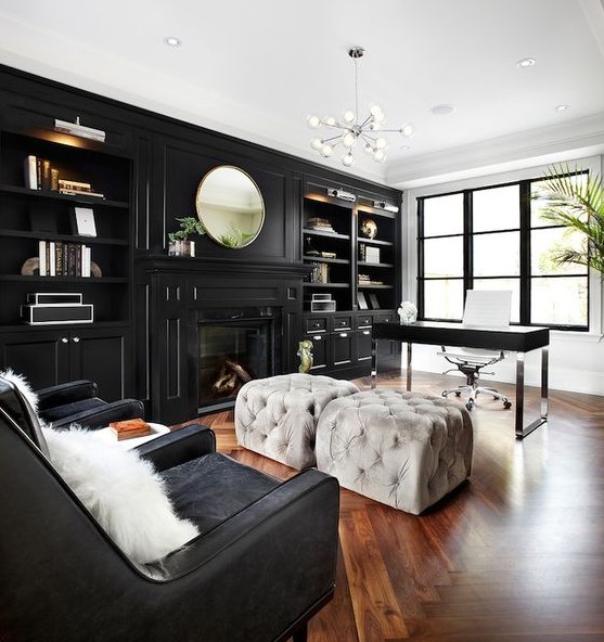 a moody home office with a glazed wall, a black storage unit with built-in shelves and a fireplace, a black desk and grey poufs, black chairs and a lovely chandelier