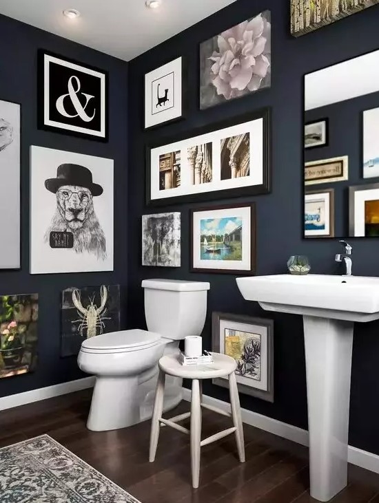 a navy bathroom with a gallery wall that takes all the blank wall space, white appliances and a mirror integrated into this art spot