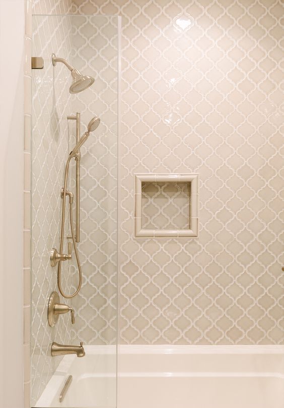 a neutral bathroom clad with tan arabesque tiles, with vintage brass fxitures and a niche shelf is all cool