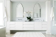 a neutral bathroom with green small scale and taupe arabesque tiles on the floor, neutral furniture, catchily shaped mirrors