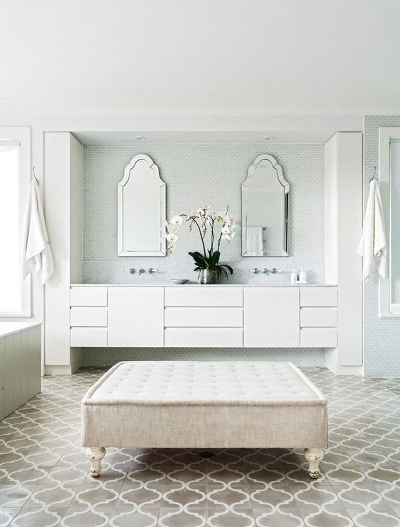 a neutral bathroom with green small scale and taupe arabesque tiles on the floor, neutral furniture, catchily shaped mirrors