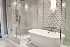 a neutral bathroom with marble and arabesque tiles, a shower space and an oval tub, lamps and built-in lights