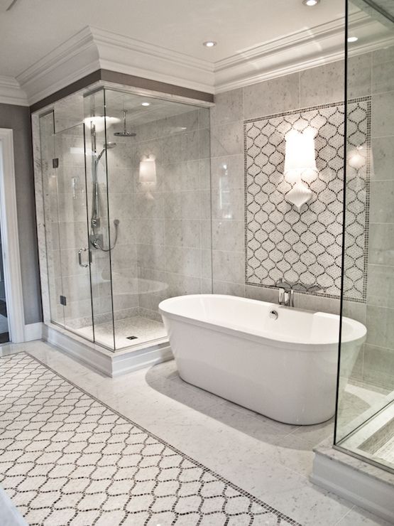 a neutral bathroom with marble and arabesque tiles, a shower space and an oval tub, lamps and built in lights