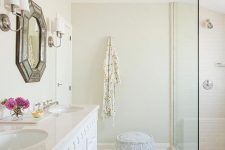 a neutral bathroom with tan walls, a white arabesque tile floor, a white vanity and a chic geometric mirror plus lamps