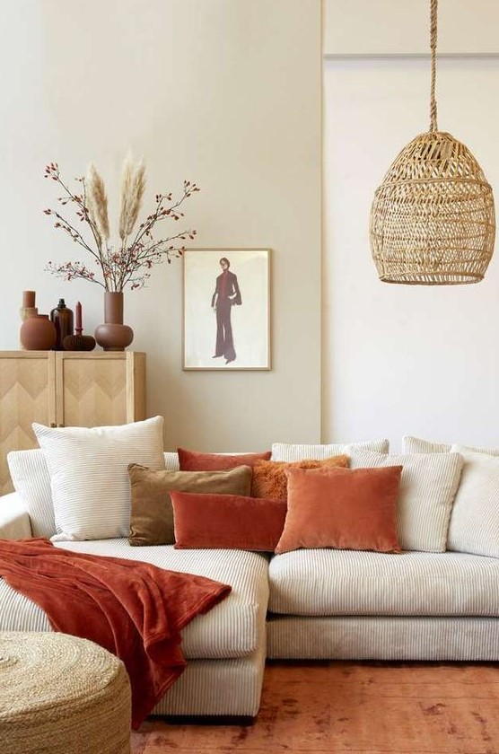 a neutral boho living room accessorized with bright rust and terracotta pillows and a woven pendant lamp is chic