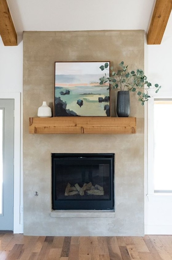 a neutral concrete fireplace with a wooden mantel, an artwork and greenery in a vase looks breezy and chic