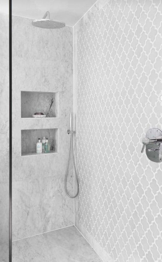 a neutral contemporary bathroom with grey arabesque and marble tiles, niche shelves and stainless steel fixtures