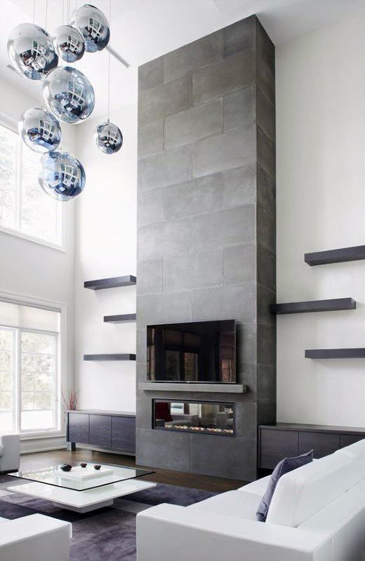 a neutral contemporary living room with a concrete fireplace, white seating furniture, a bubble chandelier and a tiered coffee table
