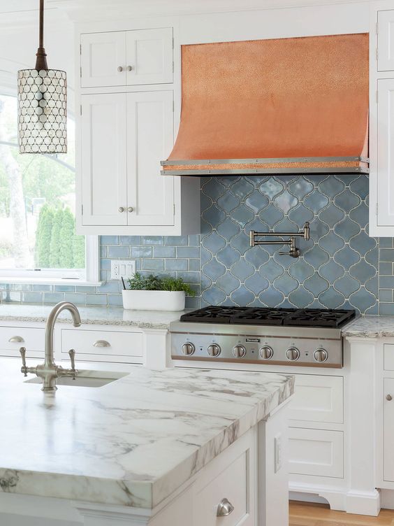 a neutral modern farmhouse kitchen with a blue subway and arabesque tile backsplash and an amber hood plus a chic pendant lamp