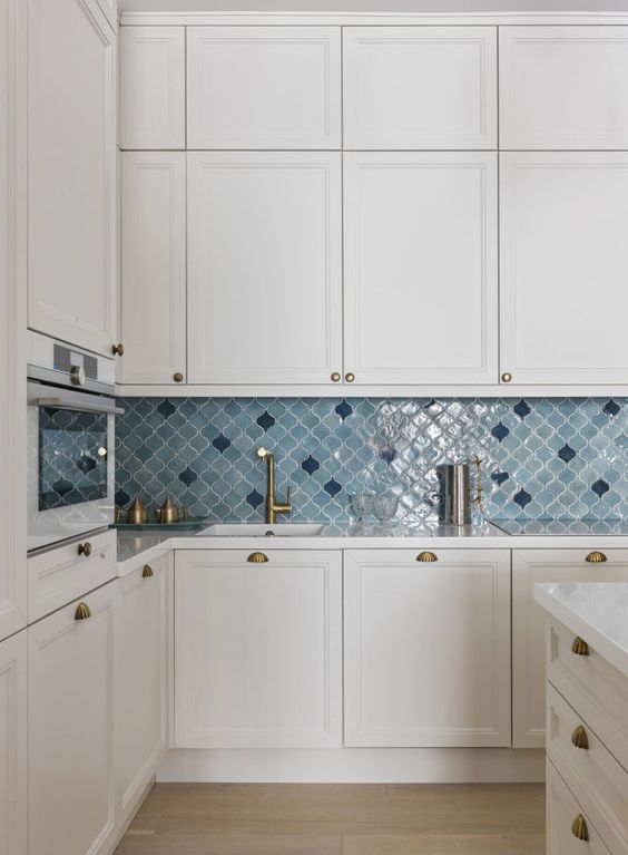 a neutral modern kitchen with shaker cabinets, a blue and navy arabesque tile backsplash and brass knobs and fixutres is amazing