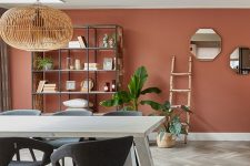 a pretty boho dining room with a terracotta accent wall, a large storage unit, a white table and grey chairs plus a wooden pendant lamp