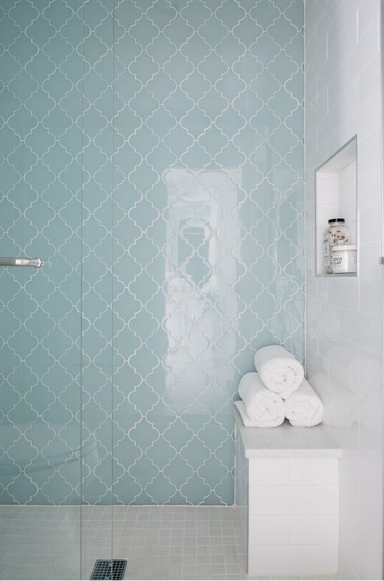 a pretty shower space done with white marble and blue arabesque tiles, with a bench and a niche for storage is a gorgeous space