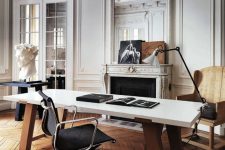 a refined and chic Parisian-inspired home office with molding, a fireplace, a stained chair, a black table, a large desk and a cool lamp