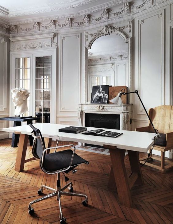 a refined and chic Parisian inspired home office with molding, a fireplace, a stained chair, a black table, a large desk and a cool lamp