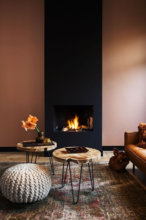 a refined modern living room with a rust-colored wall and a black fireplace, a leather sofa, wood slice tables and a knit ottoman