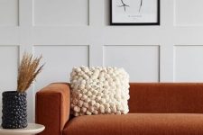 a refined modern space with off-white paneled walls, a terracotta sofa, a pompom pillow and a matching vase
