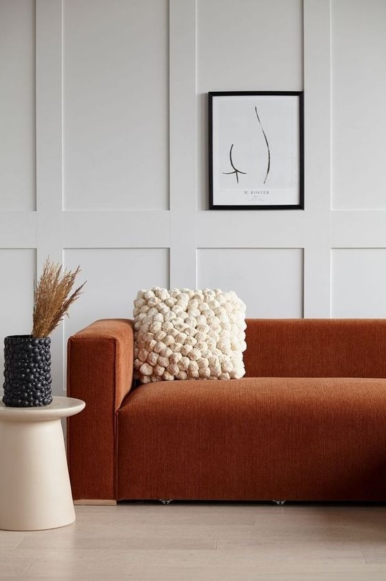 a refined modern space with off white paneled walls, a terracotta sofa, a pompom pillow and a matching vase