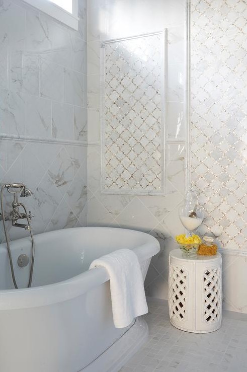 a refined white bathroom clad with white marble tiles and white arabesque tiles accented with shiny gold grout