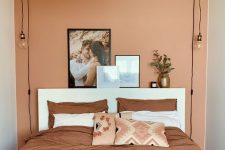 a small bedroom with a terracotta accent wall, a white bed and terracotta bedding and a large woven lamp