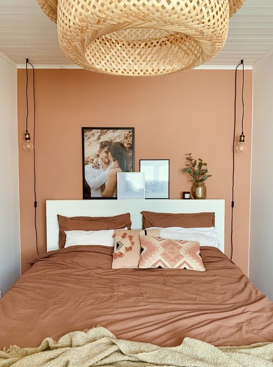 a small bedroom with a terracotta accent wall, a white bed and terracotta bedding and a large woven lamp