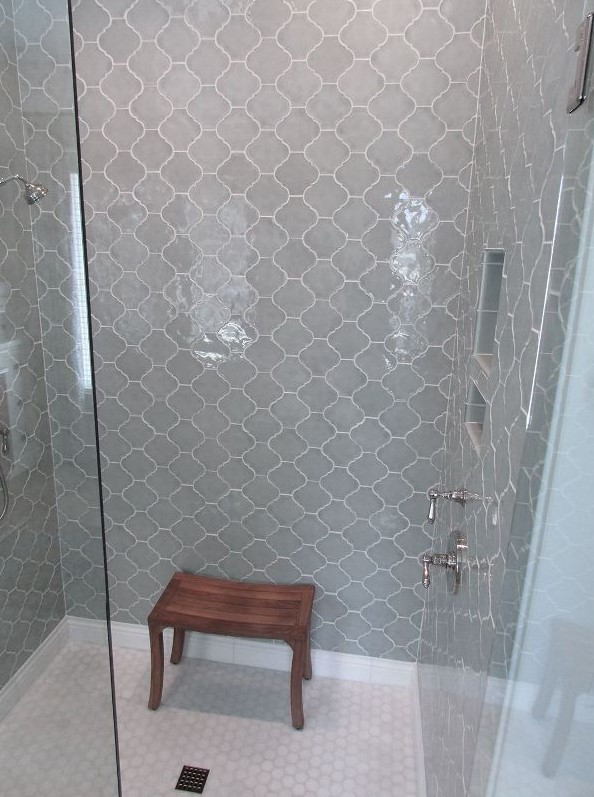a small shower space fully clad with light grey arabesque tiles and with white penny tiles on the floor looks serene and lovely