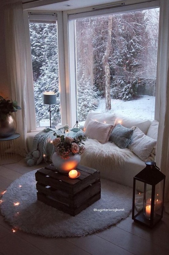 a sofa built into the space by the ay window, with lots of blankets and pillows, a crate table with blooms and candles