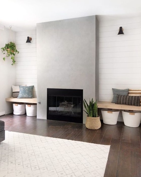 a stylish laconic living room with a concrete fireplace and benches on each side, pillows and baskets for storage