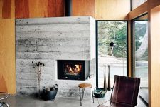 a stylish mid-century modern cabin living room with a rough concrete fireplace, a leather chair and wooden stools, a living edge table