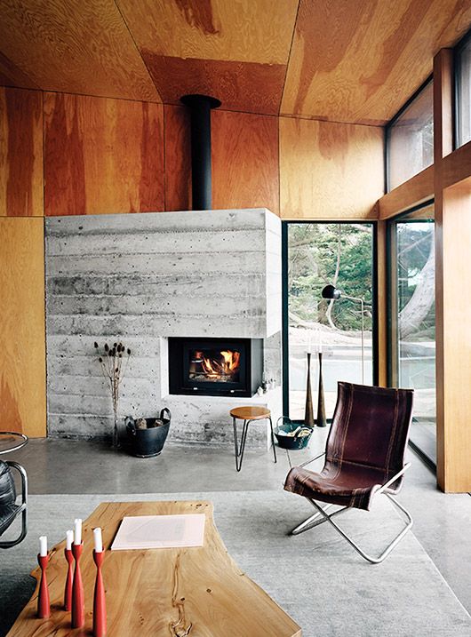 a stylish mid-century modern cabin living room with a rough concrete fireplace, a leather chair and wooden stools, a living edge table