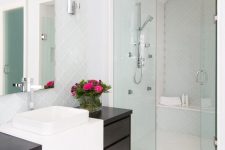 a stylish modern bathroom clad with pale blue arabesque tiles, with a dark and white vanity and a large mirror with no frame