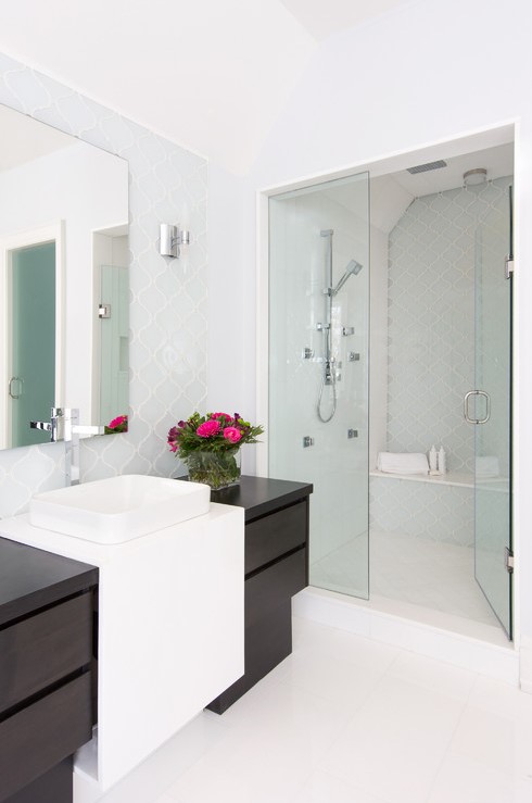 a stylish modern bathroom clad with pale blue arabesque tiles, with a dark and white vanity and a large mirror with no frame