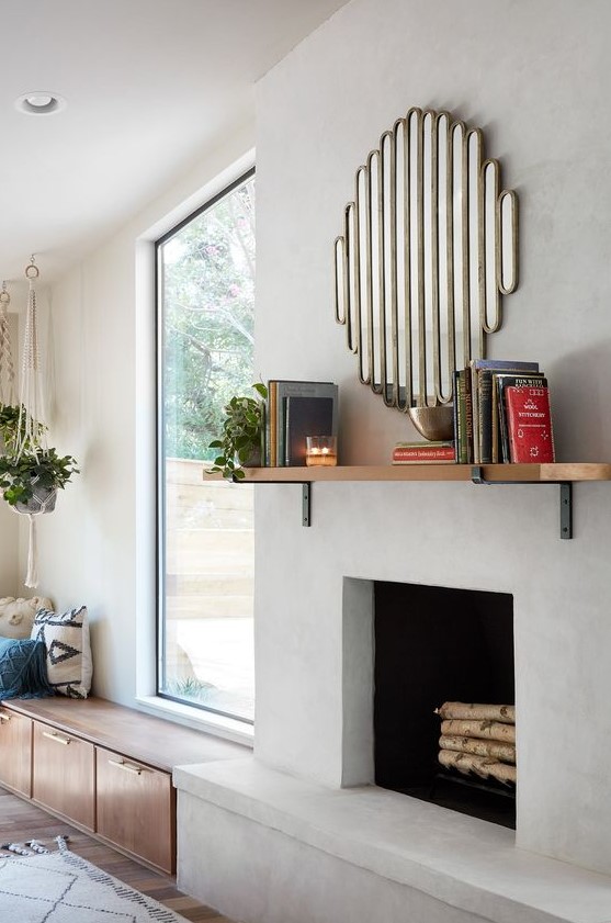a stylish modern concrete fireplace with a mantel with books and a catchy mirror over it plus a bench next to it