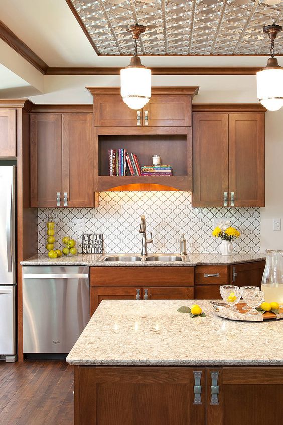 a stylish stained kitchen with a white arabesque tile backsplash, a neutral stone countertop, built-in lights and pendant lamps