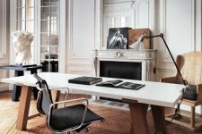 a super refined Parisian home office with molding on the walls and ceiling, an ornated fireplace, a desk, a black chair, a floor lamp and some art