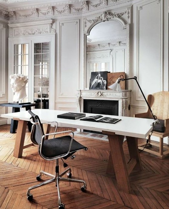 a super refined Parisian home office with molding on the walls and ceiling, an ornated fireplace, a desk, a black chair, a floor lamp and some art