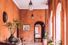 a unique boho Moroccan entryway with terracotta walls, a stained and rough wooden console table, stained chairs and potted plants
