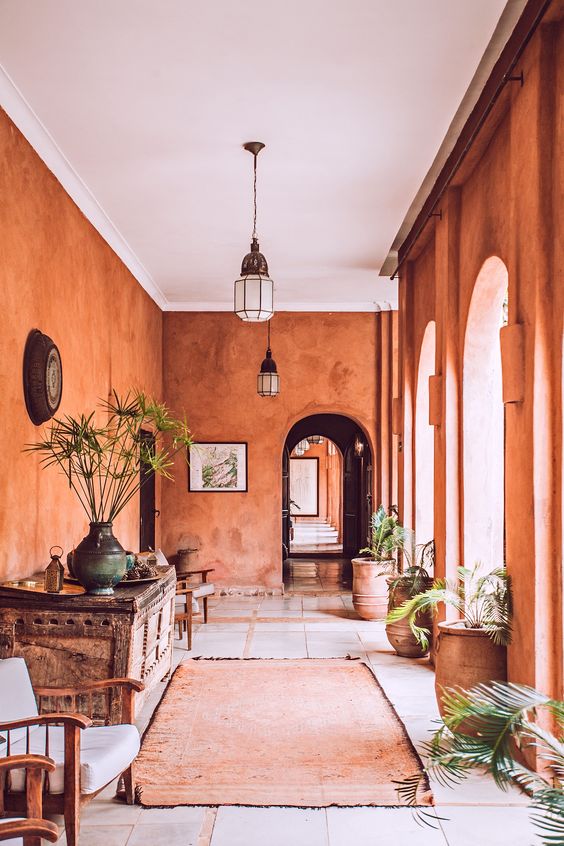 a unique boho Moroccan entryway with terracotta walls, a stained and rough wooden console table, stained chairs and potted plants