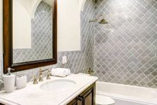 a vintage bathroom with grey arabesque tiles and mosaic ones on the floor, a stained vanity and a mirror in a stained frame